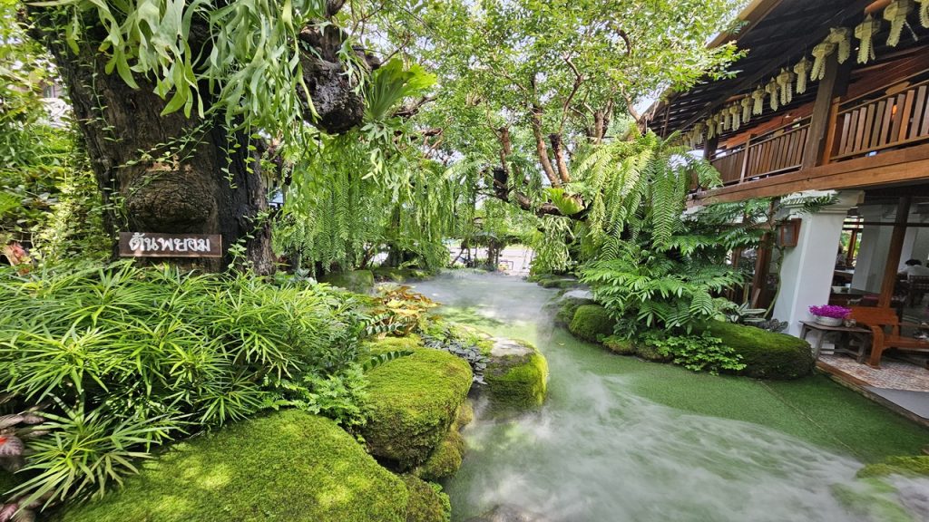 Üppiger grüner Garten mit moosbewachsenen Steinen, Farnen und Nebel zwischen tropischen Pflanzen und traditioneller Holzarchitektur – Sinnbild für organisches Wachstum und ganzheitliche Verbundenheit in der Gestalttherapie